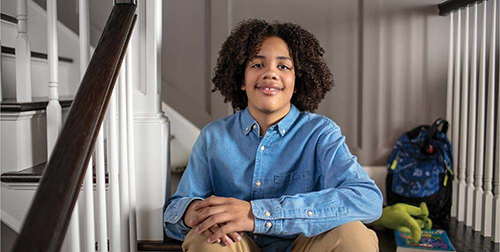 Zekeriyah smiling sitting on the steps of his home