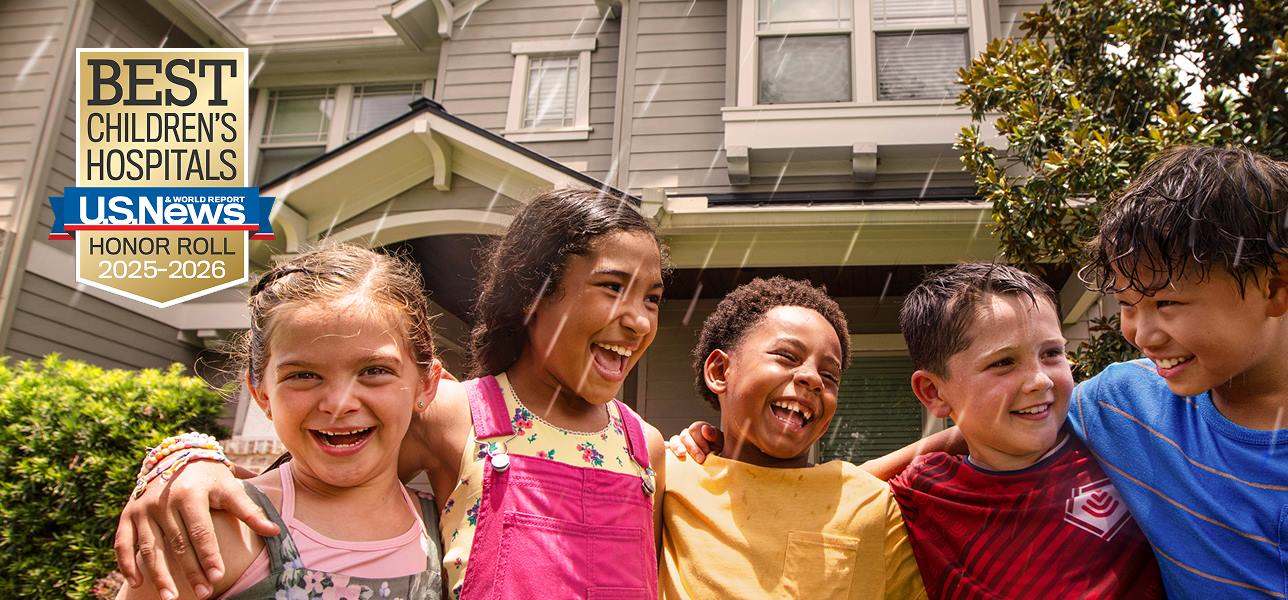 A group of five kids hugging each other beneath a sprinkler