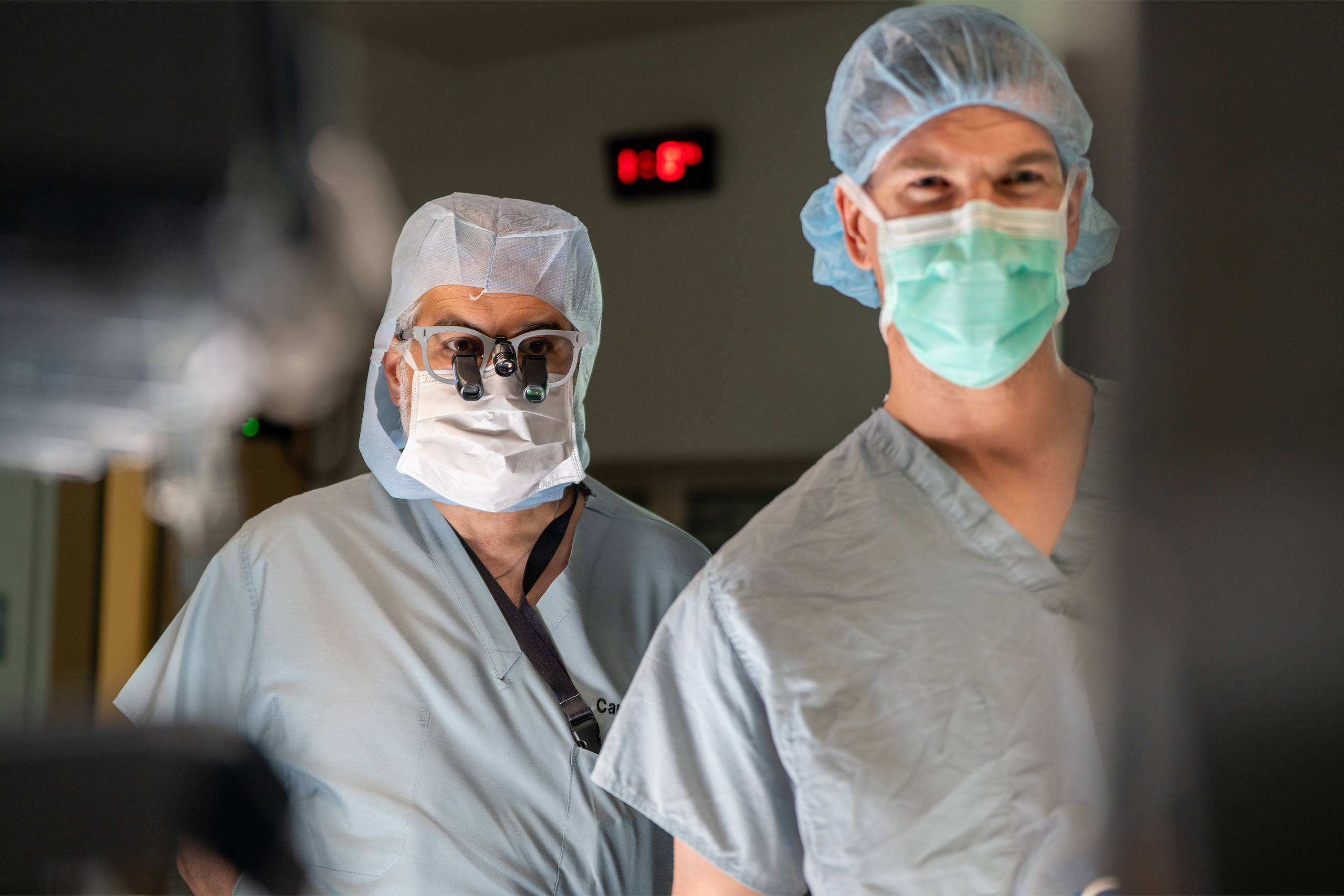 Two surgeons wearing scrubs, surgical caps, and masks in an operating room