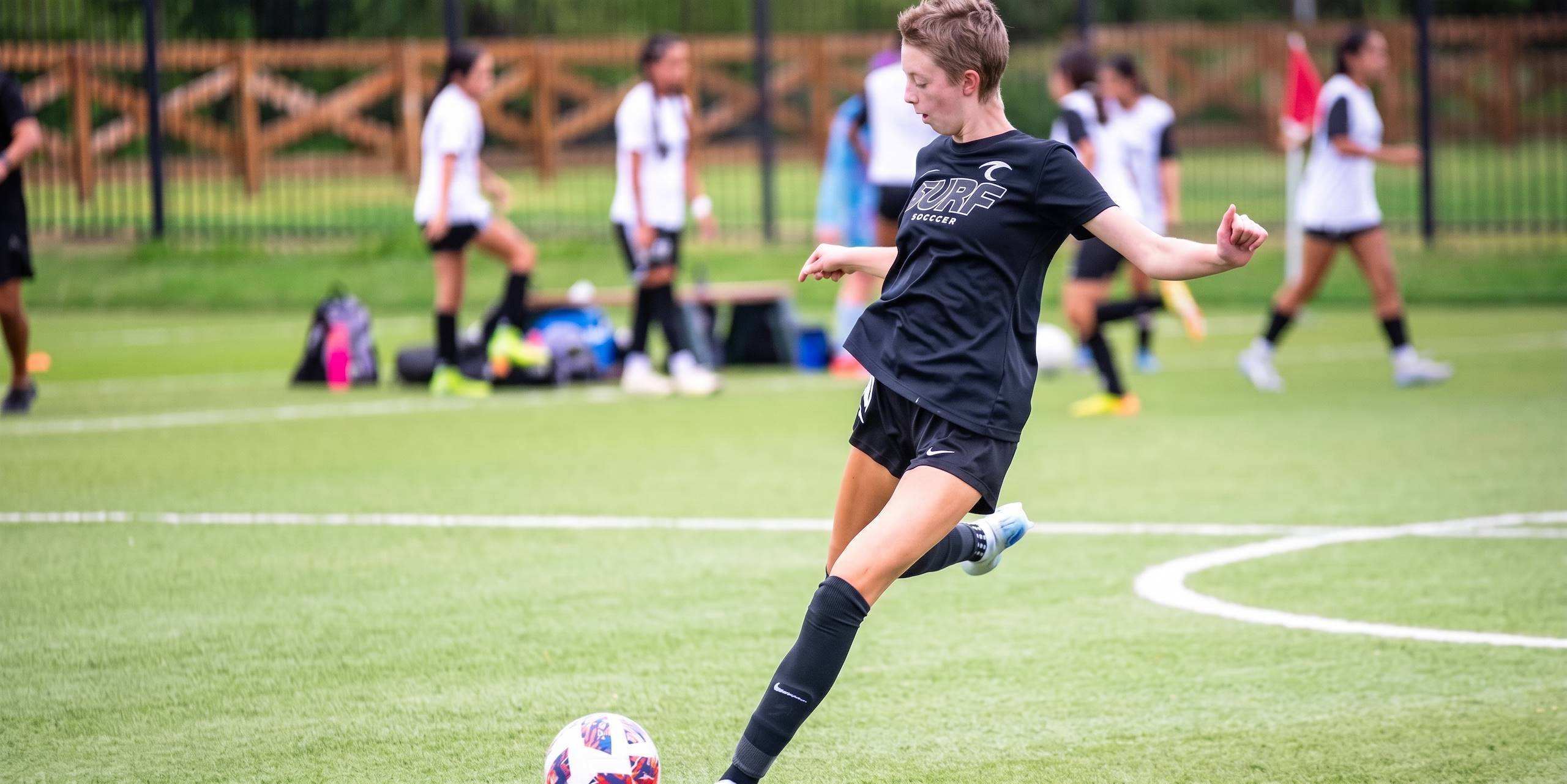A young female athlete kicking a soccer ball on a green field.