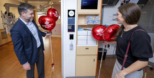 A man and a women standing outside a patient room holding red Texas Children’s balloons