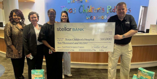 A group of corporate donors standing inside the hospital holding a giant check for $10,000 smiling at the camera