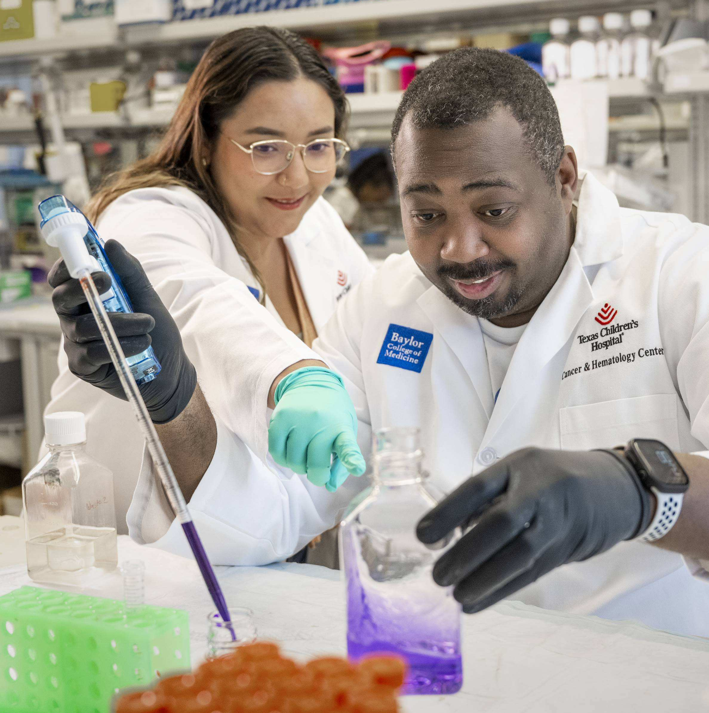 Two researchers wearing lab coats and gloves collaborating over a fluid sample on a lab bench