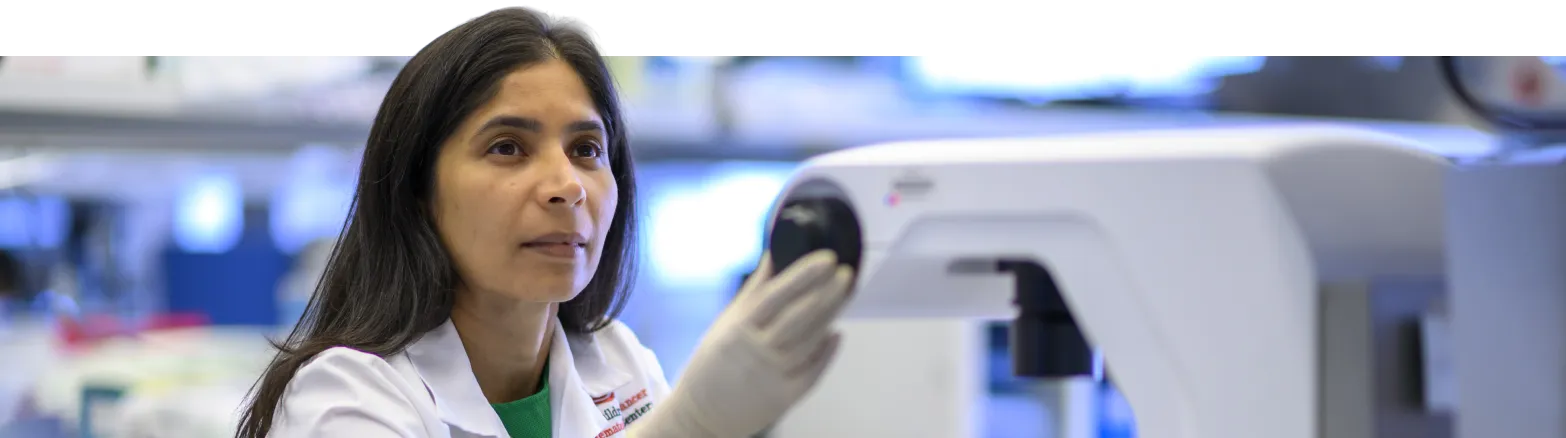 A scientist wearing a lab coat and gloves adjusts a piece of laboratory equipment in a lab setting, focusing intently on her work.